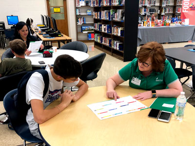 A SECU volunteer works with a high schooler at a Financial Fair, where they learn how to balance a budget in the real world.