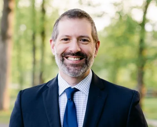 man with beard wearing dark suit smiles at camera